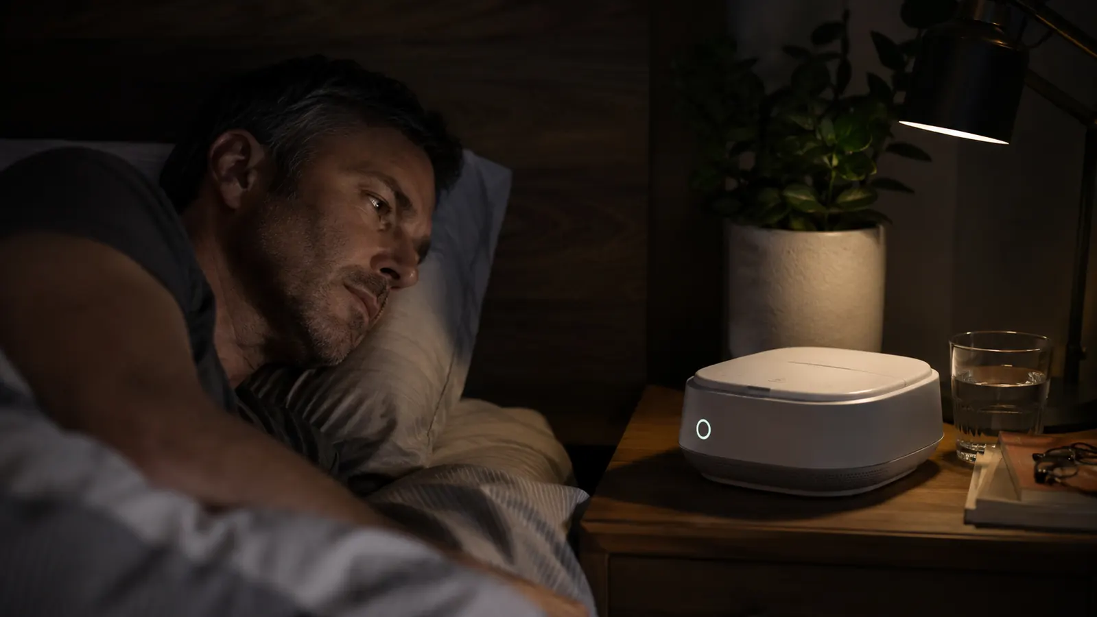 A white noise machine glowing on a nightstand in a dim room at the start of a daytime sleep shift
