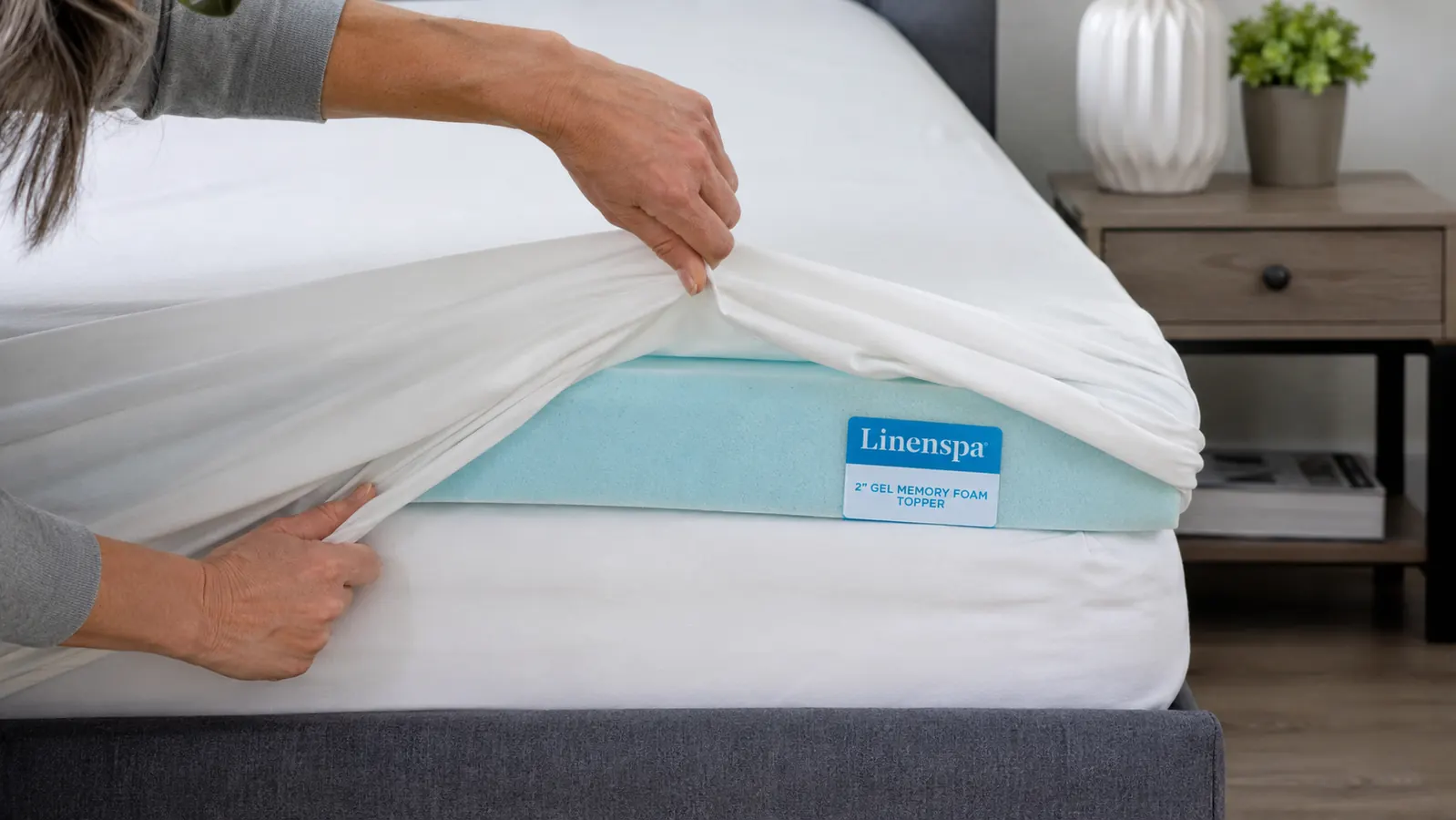 A hand smoothing the corner of a fitted sheet over the edge of the Linenspa gel memory foam topper where it has slid slightly off center