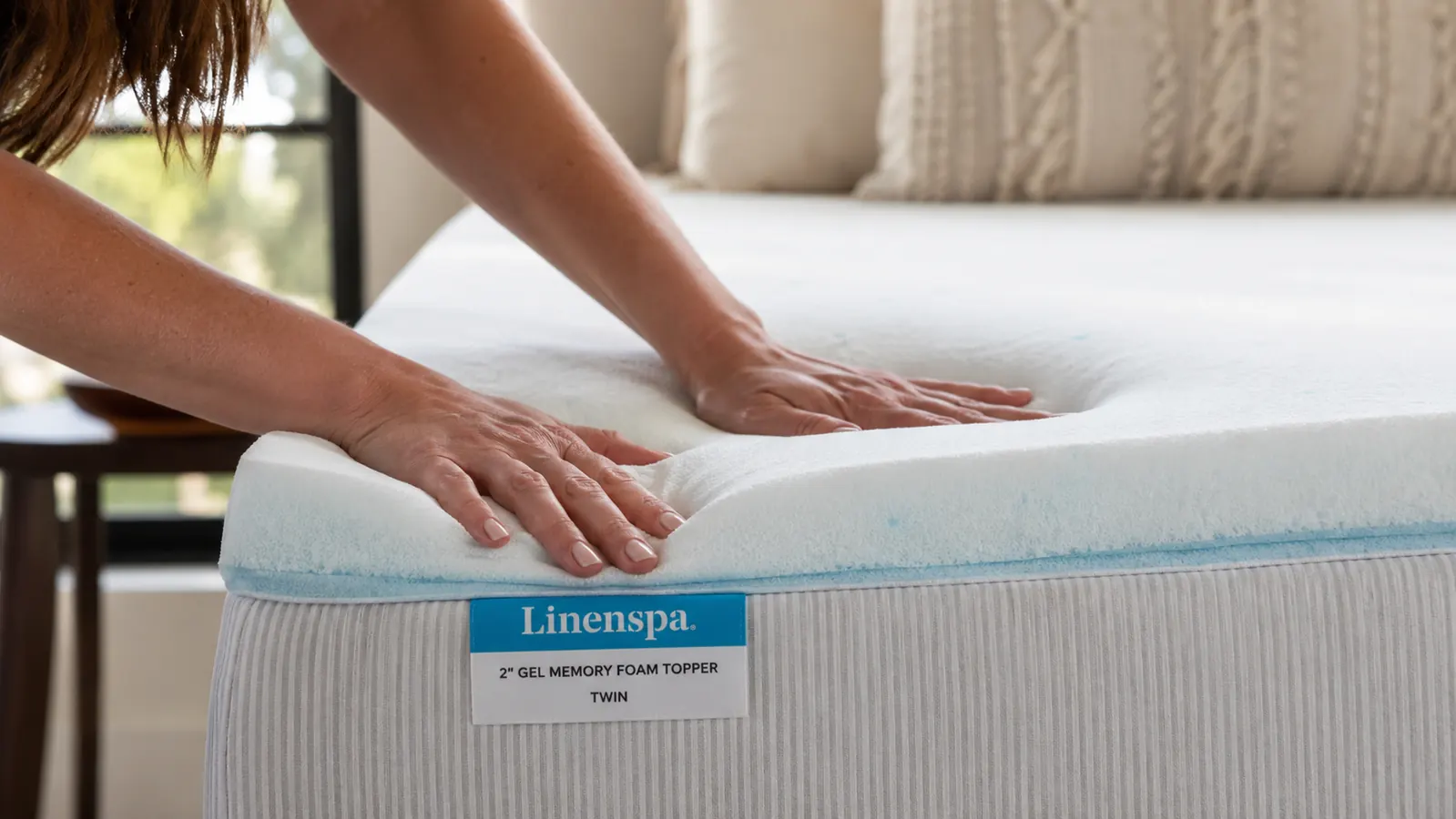 Hands pressing into the surface of the Linenspa gel memory foam mattress topper on a made bed