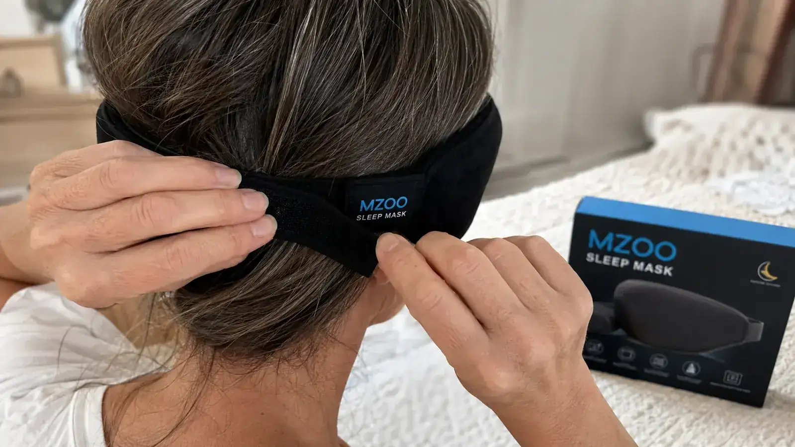 Close-up of hands adjusting the velcro strap on the back of the MZOO sleep mask to find the right notch
